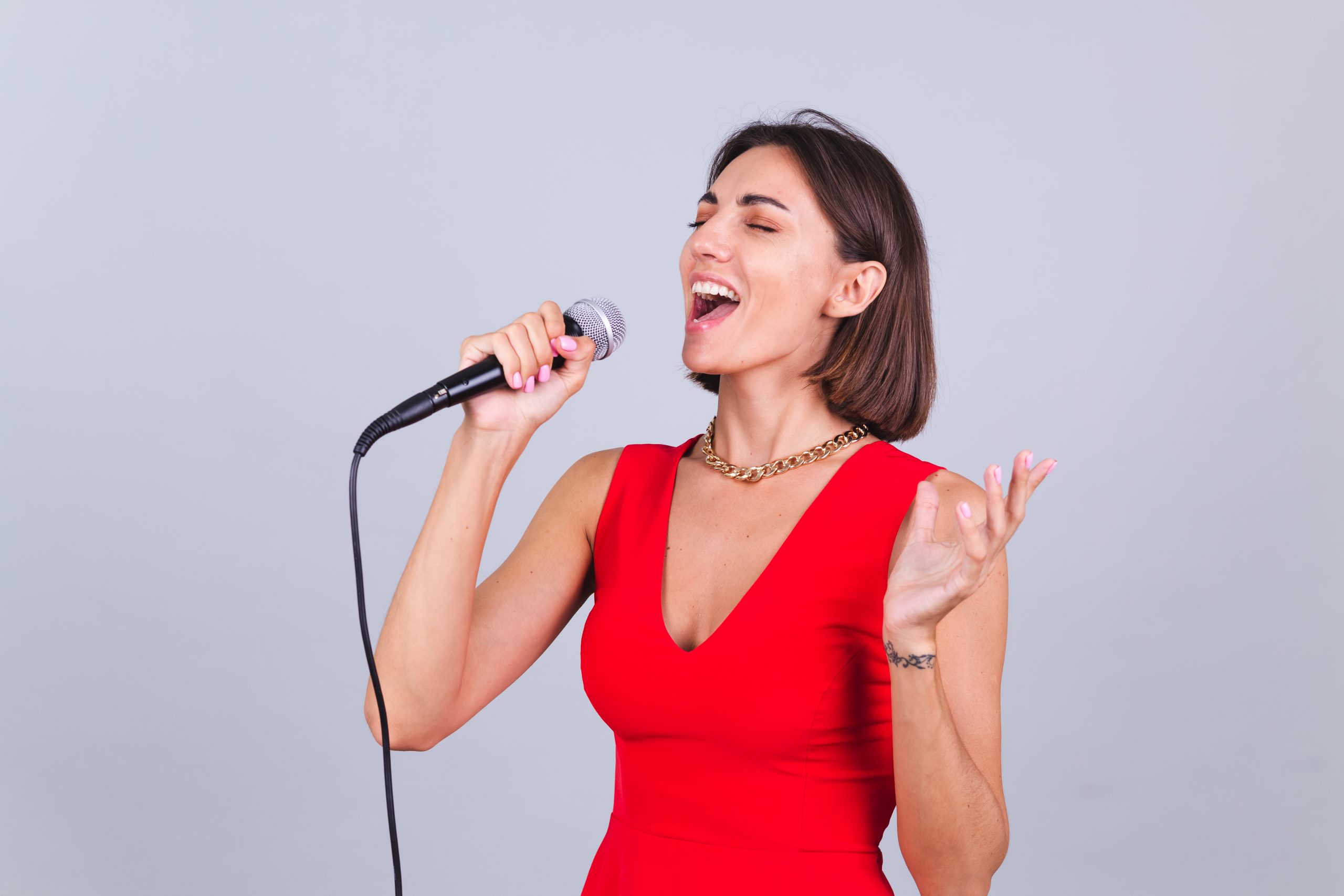 Beautiful woman on gray background with microphone singing emotional favorite song happy positive cheerful